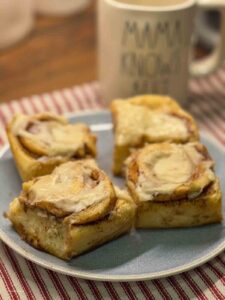 4 cinnamon rolls on a blue plate with a cup in the background